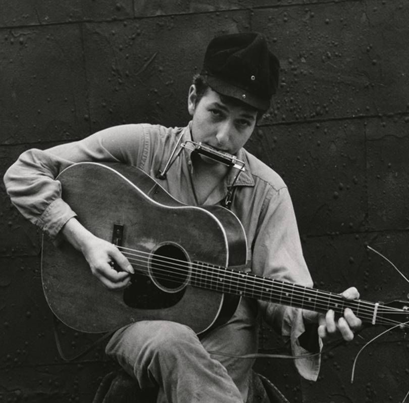 Bob Dylan lleva gorra y toca la guitarra eléctrica y la armónica