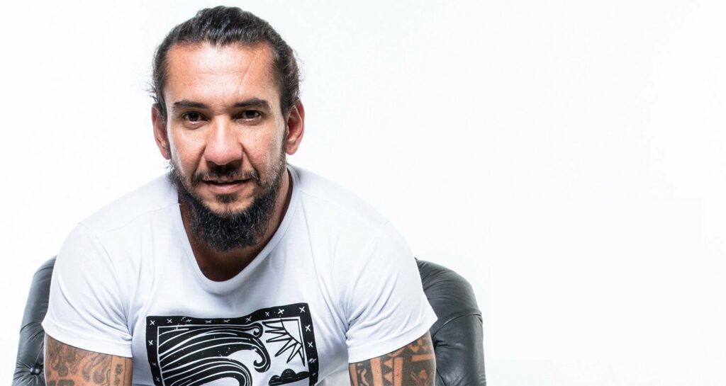 Um Rodolfo Abrantes de barba, sóbrio e mais velho sorri para a câmera