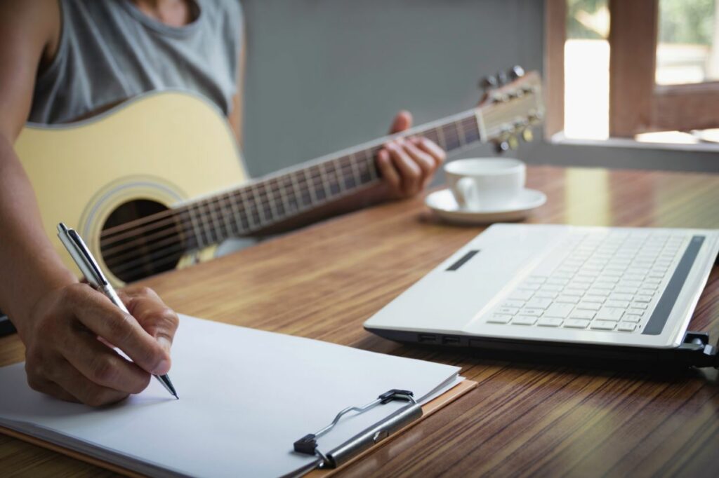 Músico segura violão e anota notas musicais na partitura
