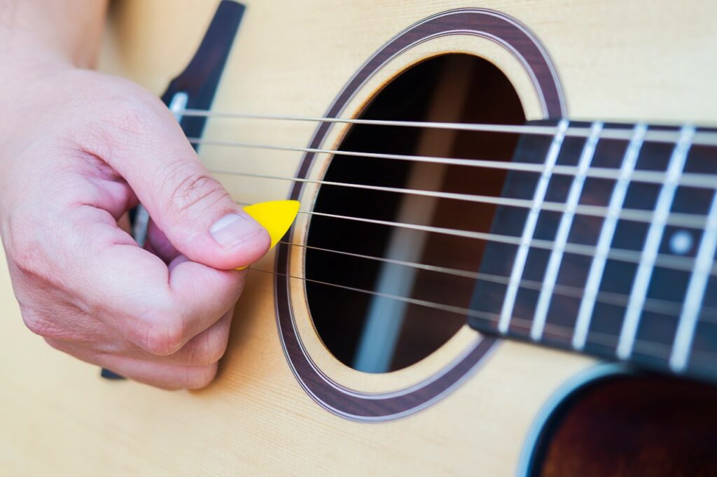Close na mão de um homem tocando violão com palheta