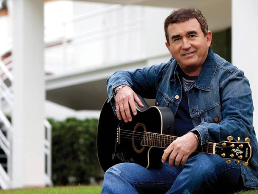 Cantor Amado Batista sentando com violão em mãos, pronto para tocar cifras de música brega