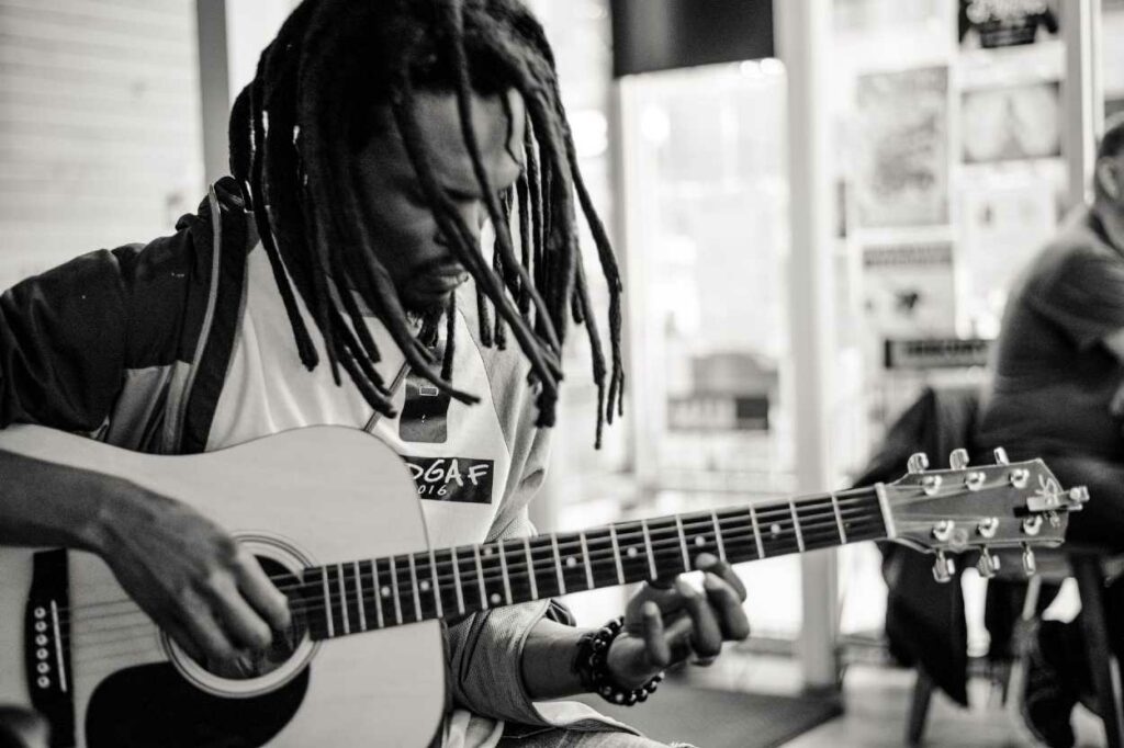 Músico negro, com cabelo rastafari, tocando arranjos em violão fingerstyle