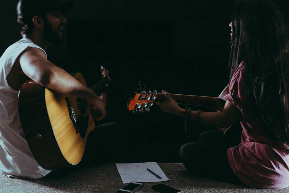 Um homem e uma mulher estudando violão sentados no chão
