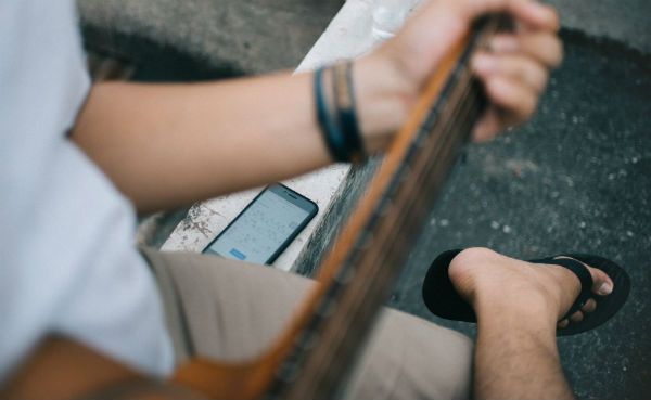 Guitarrista tocando su instrumento mientras mira una aplicación para músicos en su celular