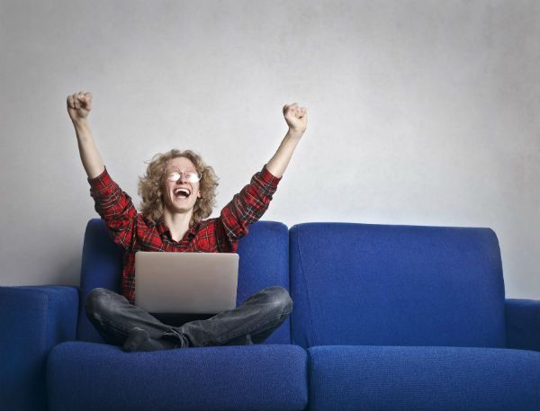 jovem_gargalhando Jovem, nerd, sentado num sofá azul e rindo diante do notebook