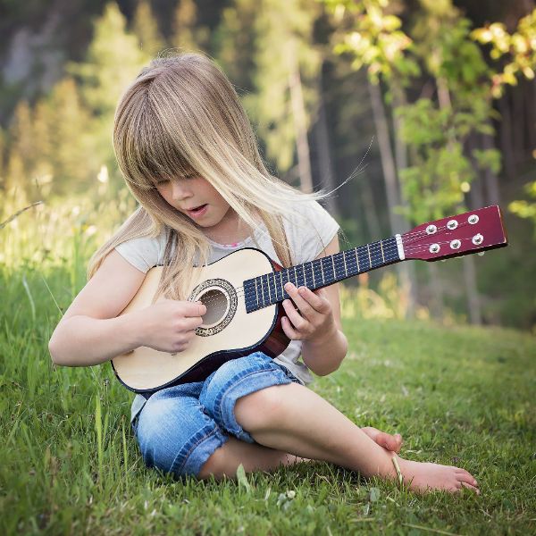 menina_tocando-violao Sentada na grama, jovem menina loira toca violão com cordas de aço