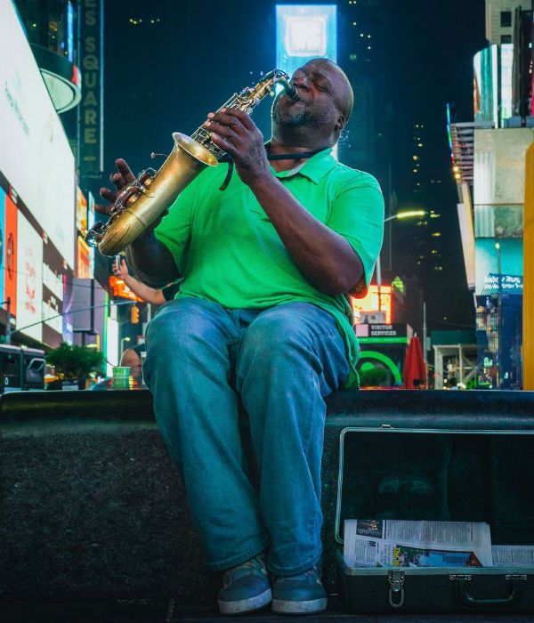 homem-tocando-saxofone Homem negro, gordo e mais velho toca saxofone, sentando em um banco de praça