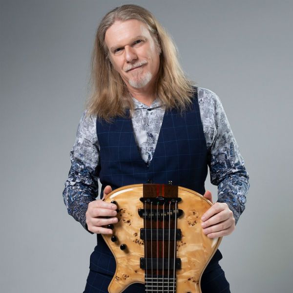 humberto-gessinger_baixista De pé, o músico Humberto Gessinger seguro um baixo de seis cordas virado de ponta à cabeça