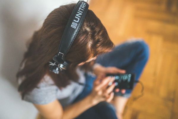 Garota jovem ouve música, no fone de ouvido, sentada no chão de sua casa
