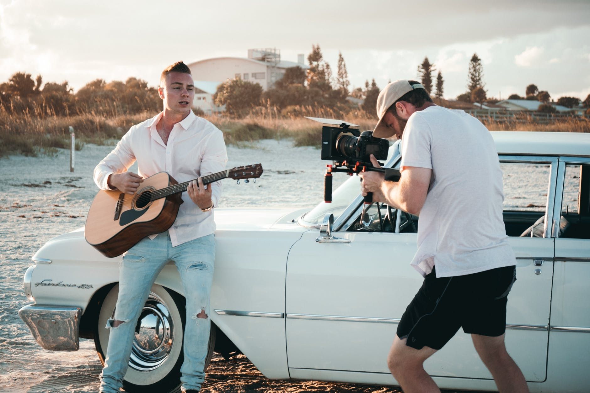 Músico sendo filmado, na praia, enquanto toca violão
