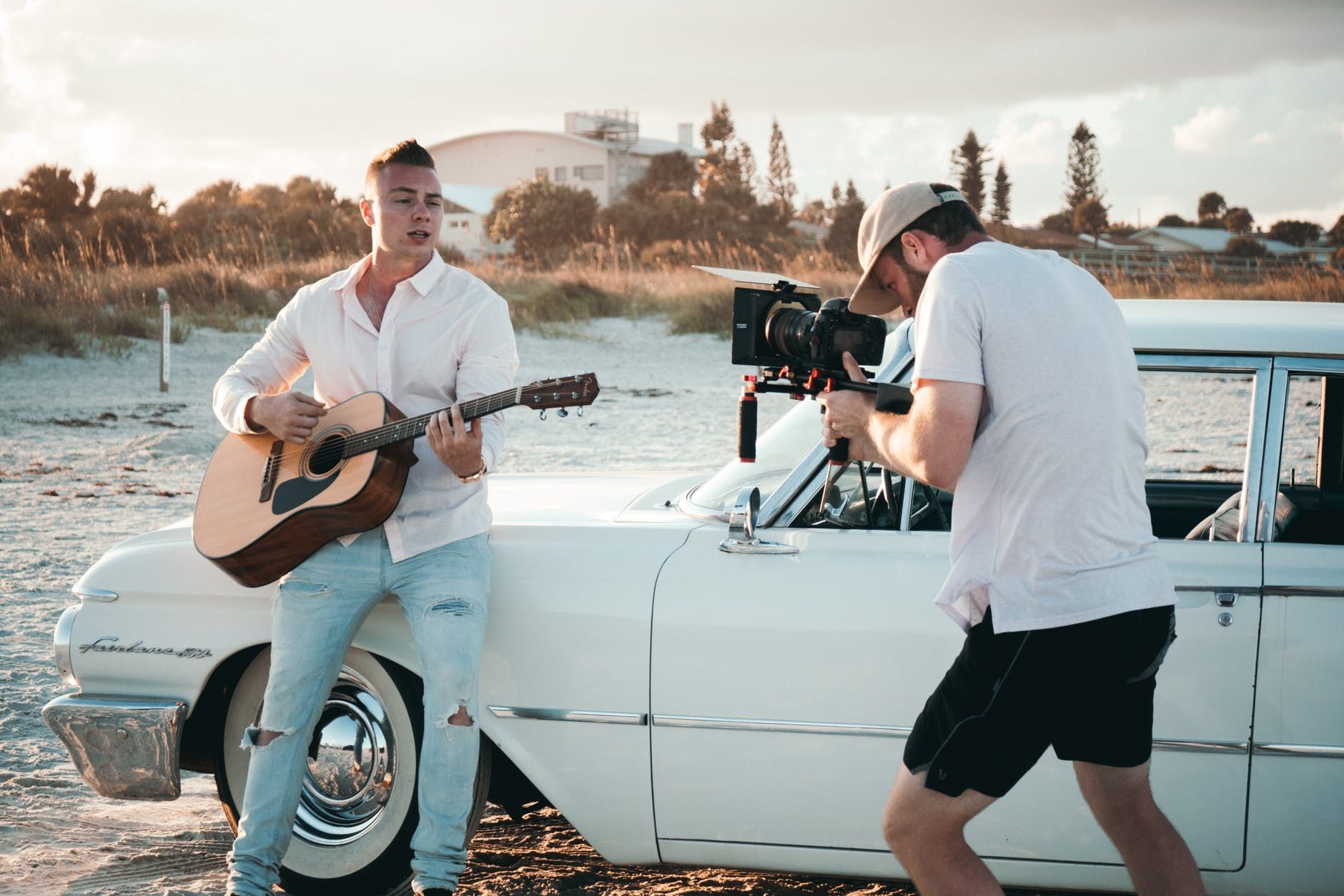 Músico sendo filmado, na praia, enquanto toca violão 